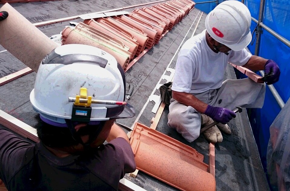屋根の上でフランス瓦施工中の職人
